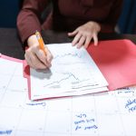 Person writing on a financial document on an organized desk with a calendar.