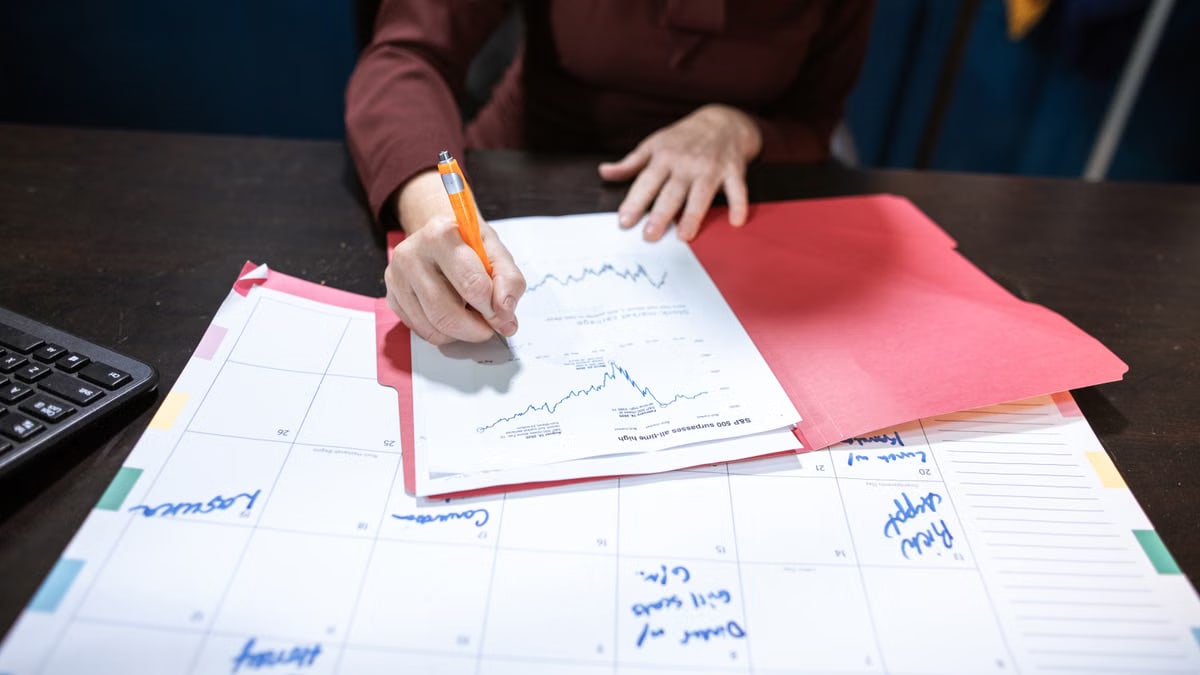 Person writing on a financial document on an organized desk with a calendar.